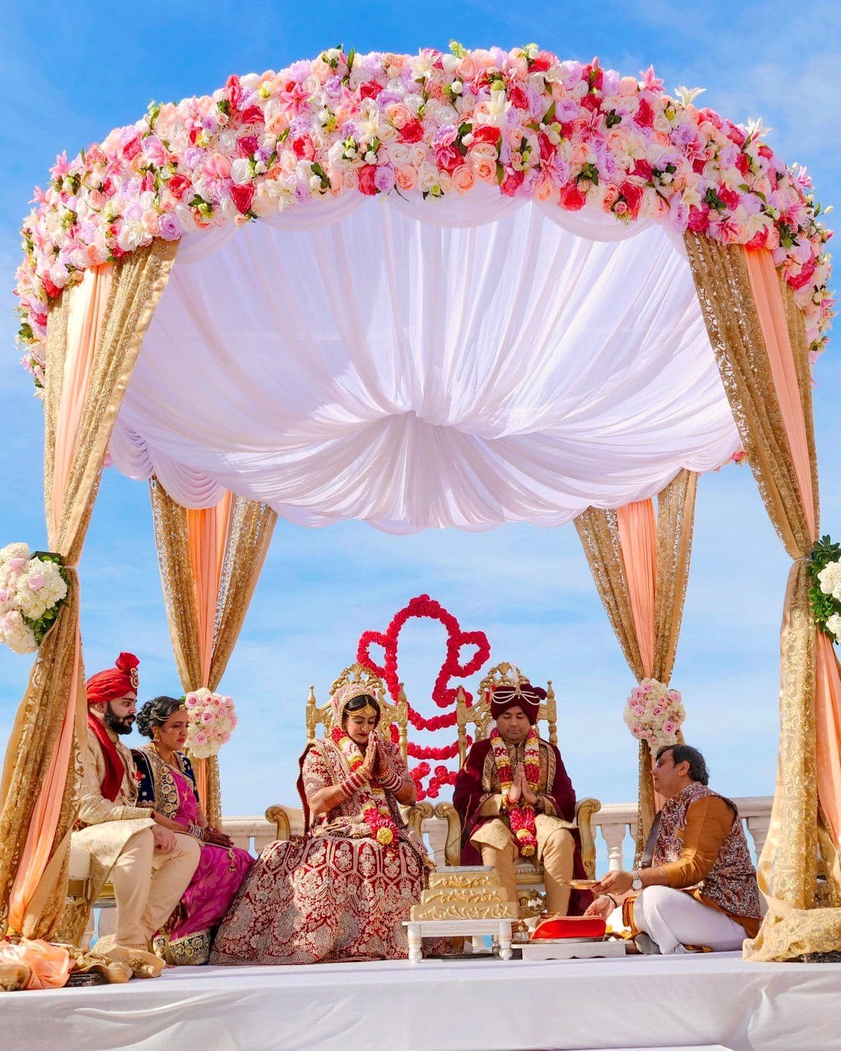 Couple seated beneath a floral mandap during the ceremony