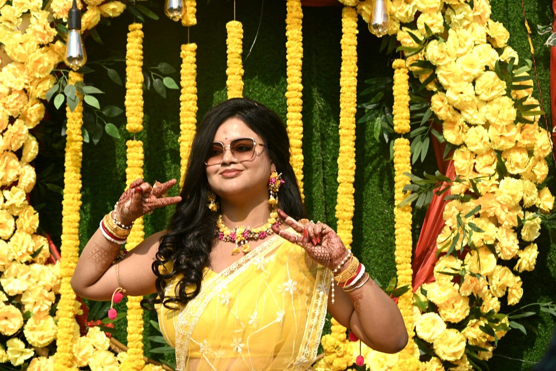 Guest in yellow beside a floral backdrop at a haldi function