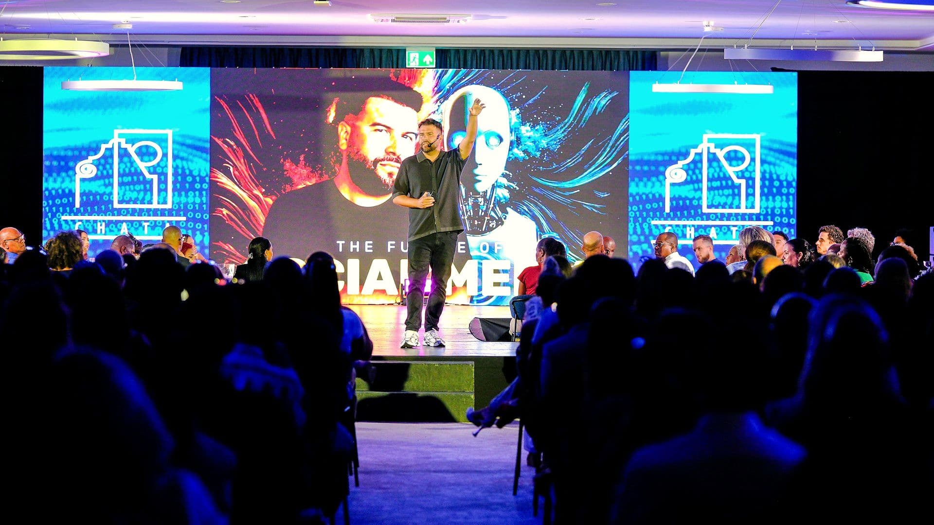 Speaker presenting on stage to a seated corporate audience