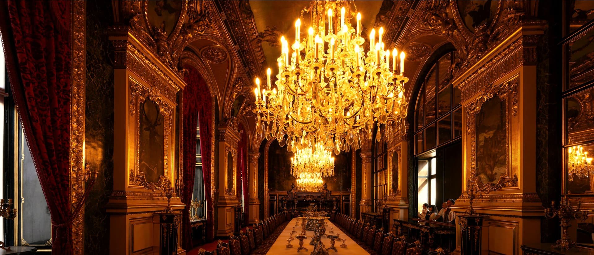 Ornate hall set with a long table beneath chandeliers